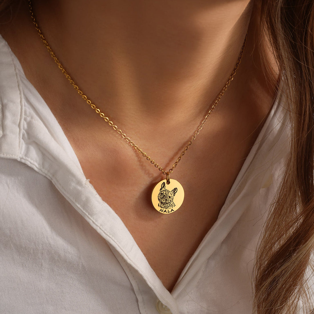 Gold necklace with a round pendant worn by a person in a white shirt.